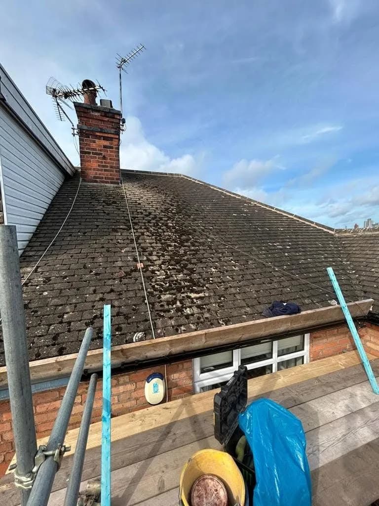 The rear roof before work: aged concrete tiles thick with moss and algae, a brick chimney stack with a television aerial, and a flat-roofed extension below, with scaffold poles along the wall.