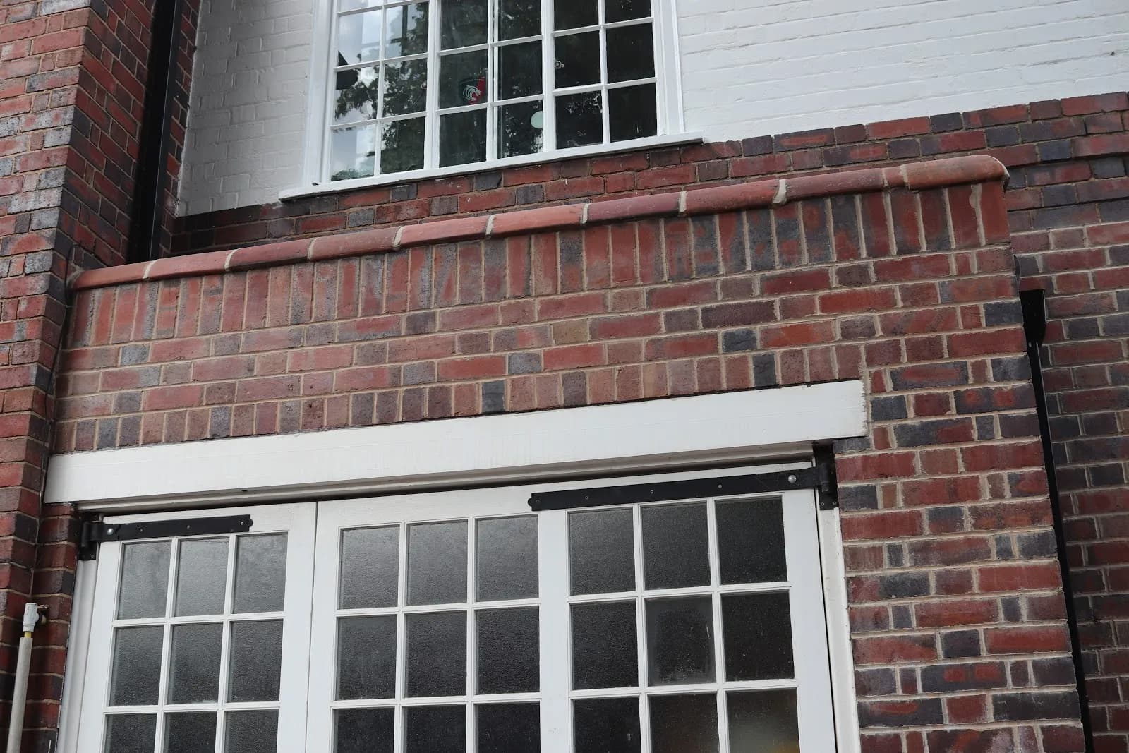 A repointed brick parapet with a rebuilt brick-on-edge coping, above a white-framed workshop window and a Georgian-bar window.